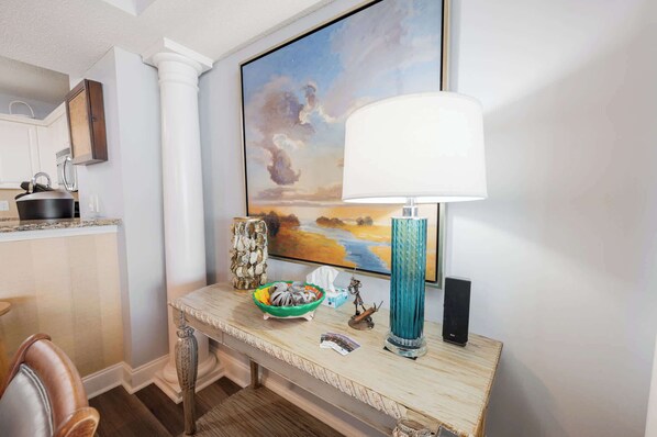 Et køkken med bordplade, vask, komfur, en dekorativ skål, en vase, et indrammet maleri og en bordlampe.