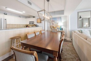 Un comedor amplio con una larga mesa de madera, armarios blancos y una cocina al fondo.