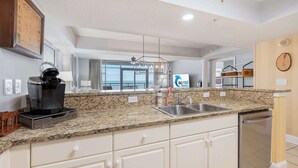 A kitchen with granite countertops, white cabinets, a coffee maker, a sink, and a dishwasher. - Ocean-view condo with balcony & beach access (Myrtle Beach)