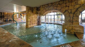 An indoor pool with stone arches, a water fountain, and a clear view of the outdoors. - Ocean-view condo with balcony & beach access (Myrtle Beach)