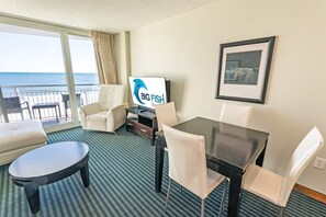 Hotellihuone, jossa on parveke, ruokailutila, televisio ja seinällä oleva taulu.