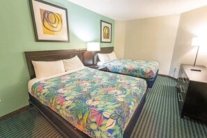 Hotellihuone, jossa on kaksi sänkyä, ja molemmissa on värikkäät, kukkakuviolliset vuodevaatteet. Huoneessa on myös yöpöytä, jossa on lamppu, sekä taideteoksia seinillä.