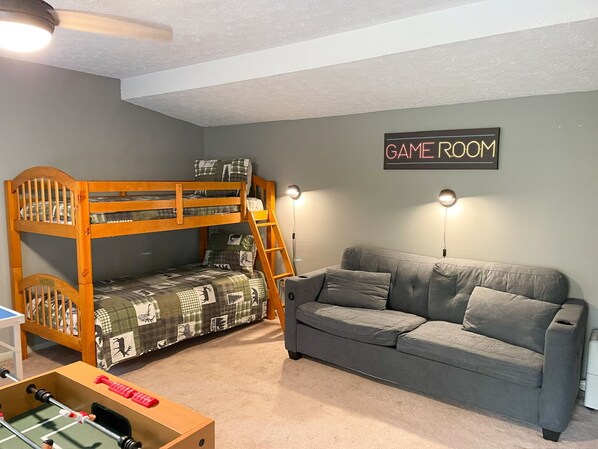 Una habitación con una cama individual superpuesta, un sofá gris y un letrero que dice 'GAMEROOM'.