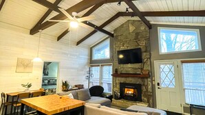 A spacious living room with a stone fireplace, wooden ceiling beams, and a large window. - Spacious 3BR/3BA Cabin Only 0.5 Miles From Slopes! (Beech Mountain)