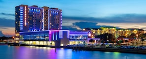 A multi-story hotel with illuminated signage, a waterfront view, and a parking lot.