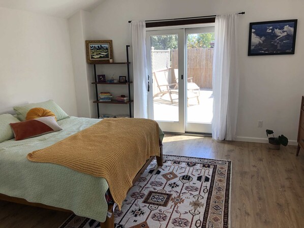 A bedroom with a bed, a bookshelf, a sliding glass door to the patio, and a patterned rug.
