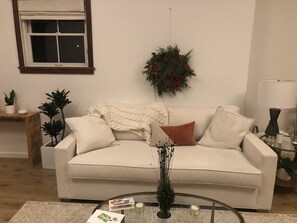 A living room with a beige sofa, a glass coffee table, and a wall-mounted wreath.