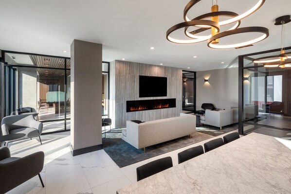 A modern living room with a fireplace, a large flat-screen TV, and a contemporary chandelier. - Global Luxury Suites At The Arches (Bronx)