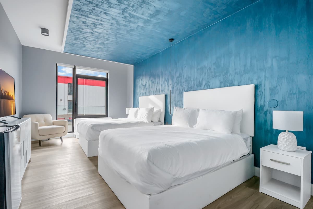 Une chambre d’hôtel moderne équipée de deux lits, d’un bureau, d’une chaise et d’une grande fenêtre.
