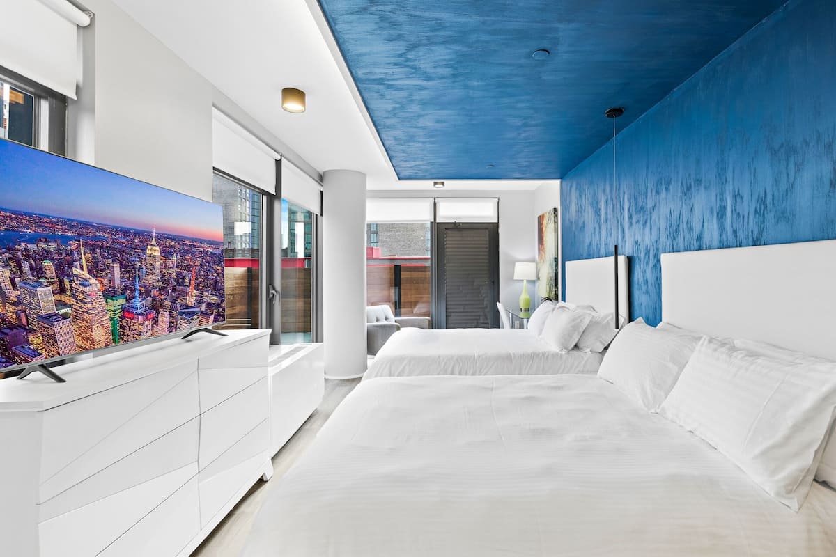 Une chambre d’hôtel moderne avec un tableau représentant un paysage urbain, un lit blanc et un mur d’accent bleu.