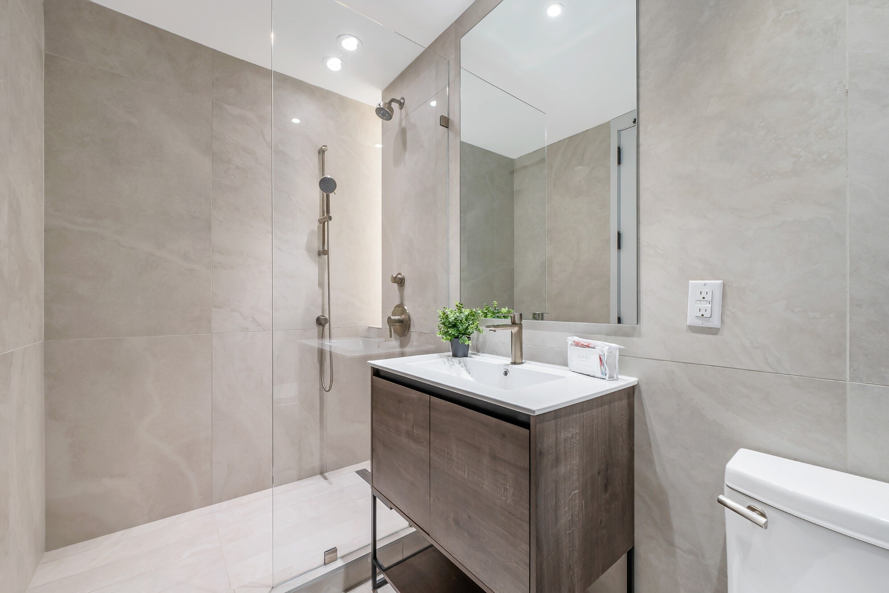 A modern bathroom with a glass shower enclosure, a wooden vanity, and a white toilet.