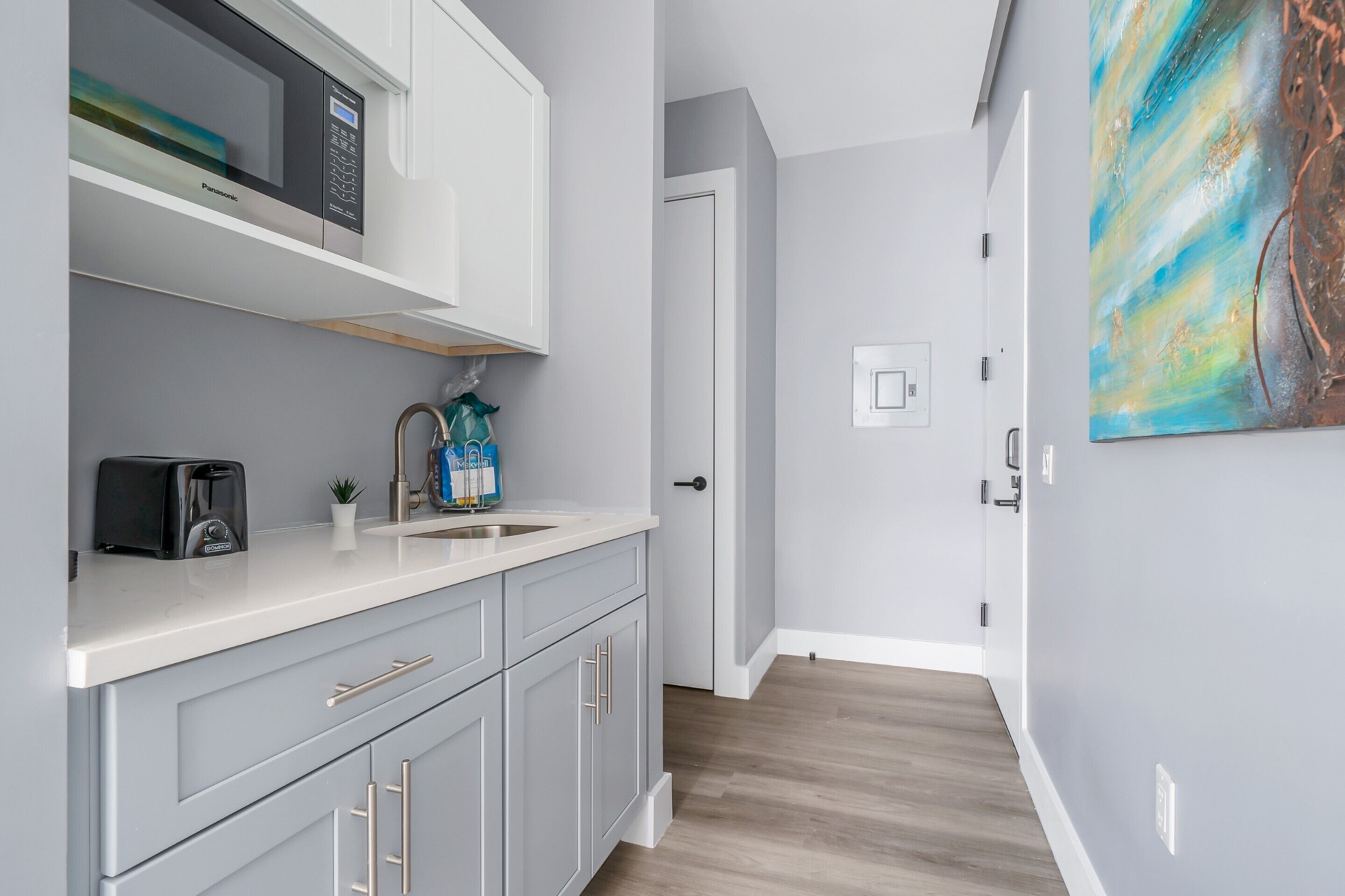 A modern kitchen with grey cabinets, a white countertop, and a microwave.