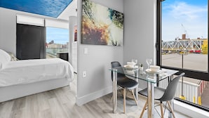 Een moderne hotelkamer met een bed, een glazen eettafel en een groot raam met uitzicht op de stad.