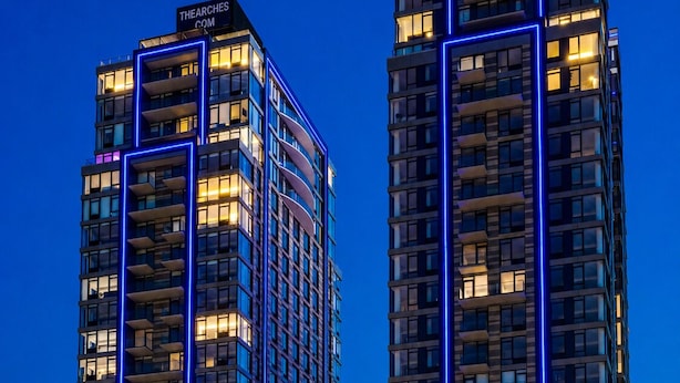 Twee hoogbouwgebouwen met verlichte blauwe lijnen, een zichtbare wateropslag en een bord dat een restaurant aangeeft.