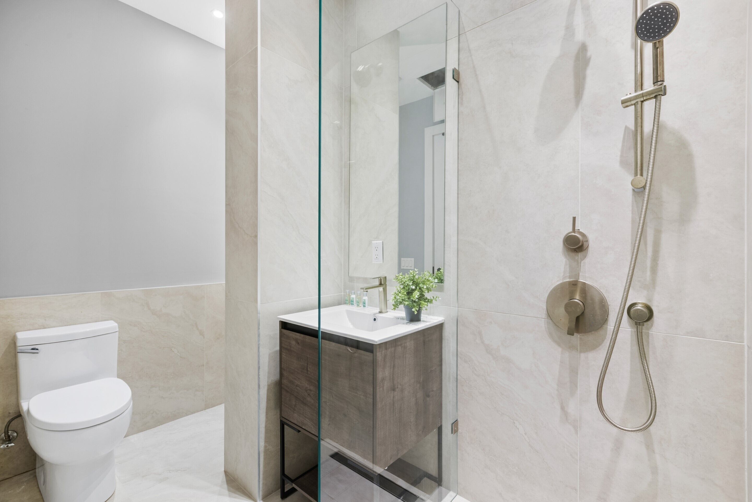 A modern bathroom with a glass-enclosed shower, a white toilet, and a vanity with a mirror and sink.