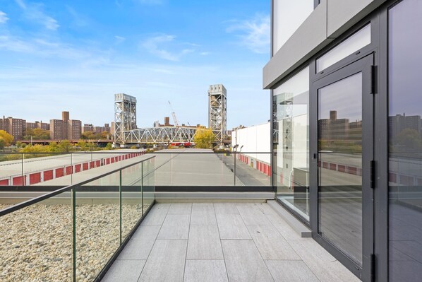 Un edificio moderno con un balcón de vidrio que da a una zona de construcción y vistas de la ciudad.