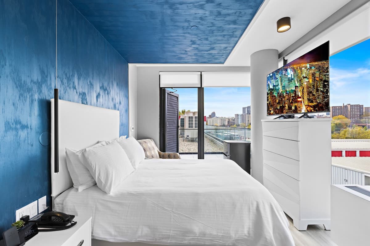 Une chambre moderne avec vue sur la ville, un grand lit, une table de chevet avec un téléphone et un téléviseur fixé au mur.