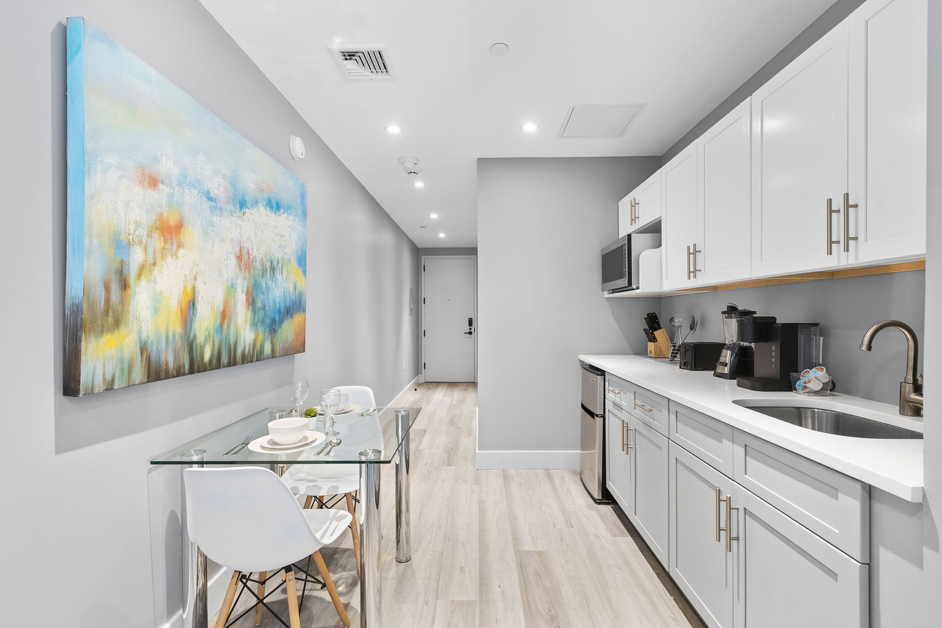 Una cocina moderna con armarios blancos, un lavamanos de acero inoxidable y una mesa de comedor de vidrio.