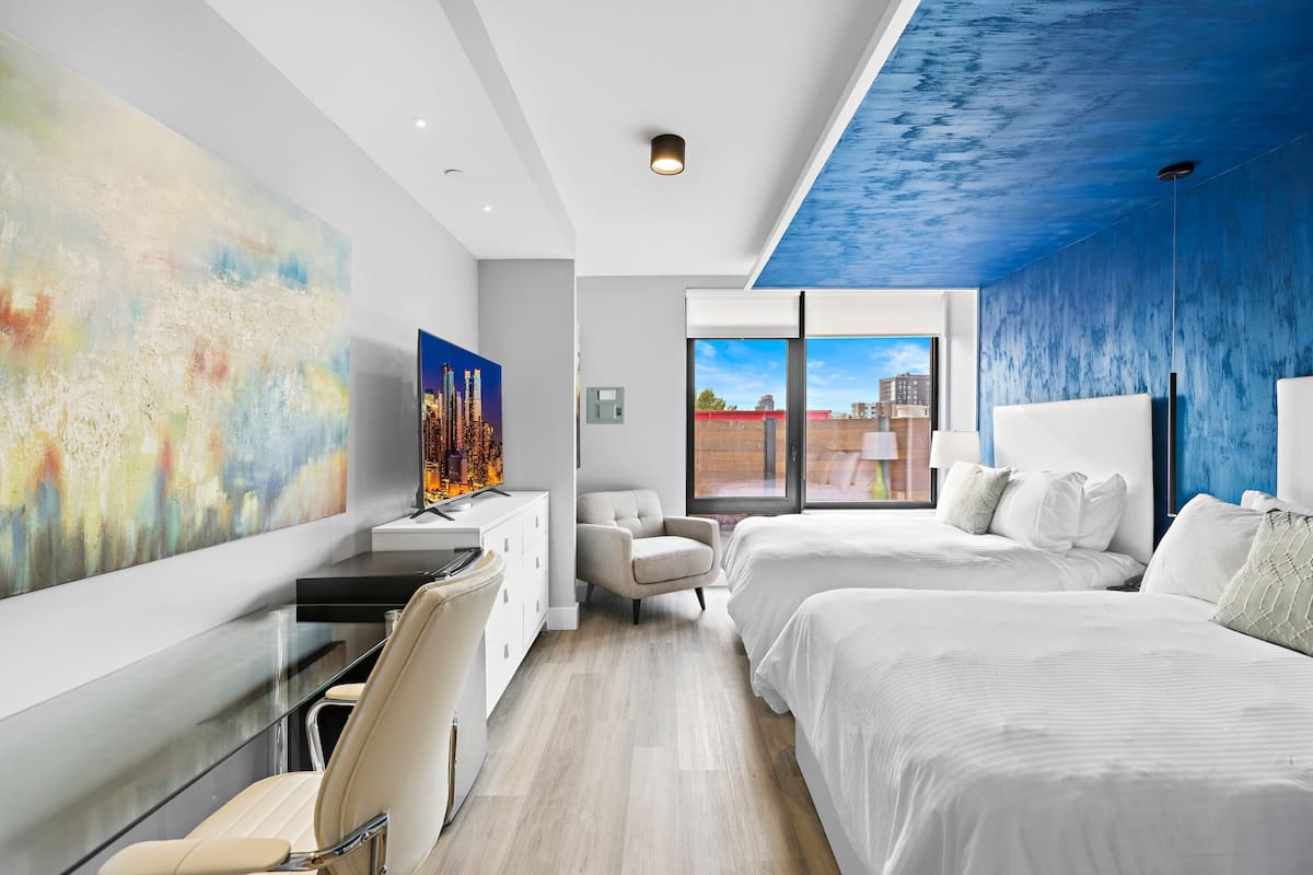 Une chambre d’hôtel moderne avec un grand tableau abstrait, une vue sur la ville, un bureau avec une chaise et deux lits.