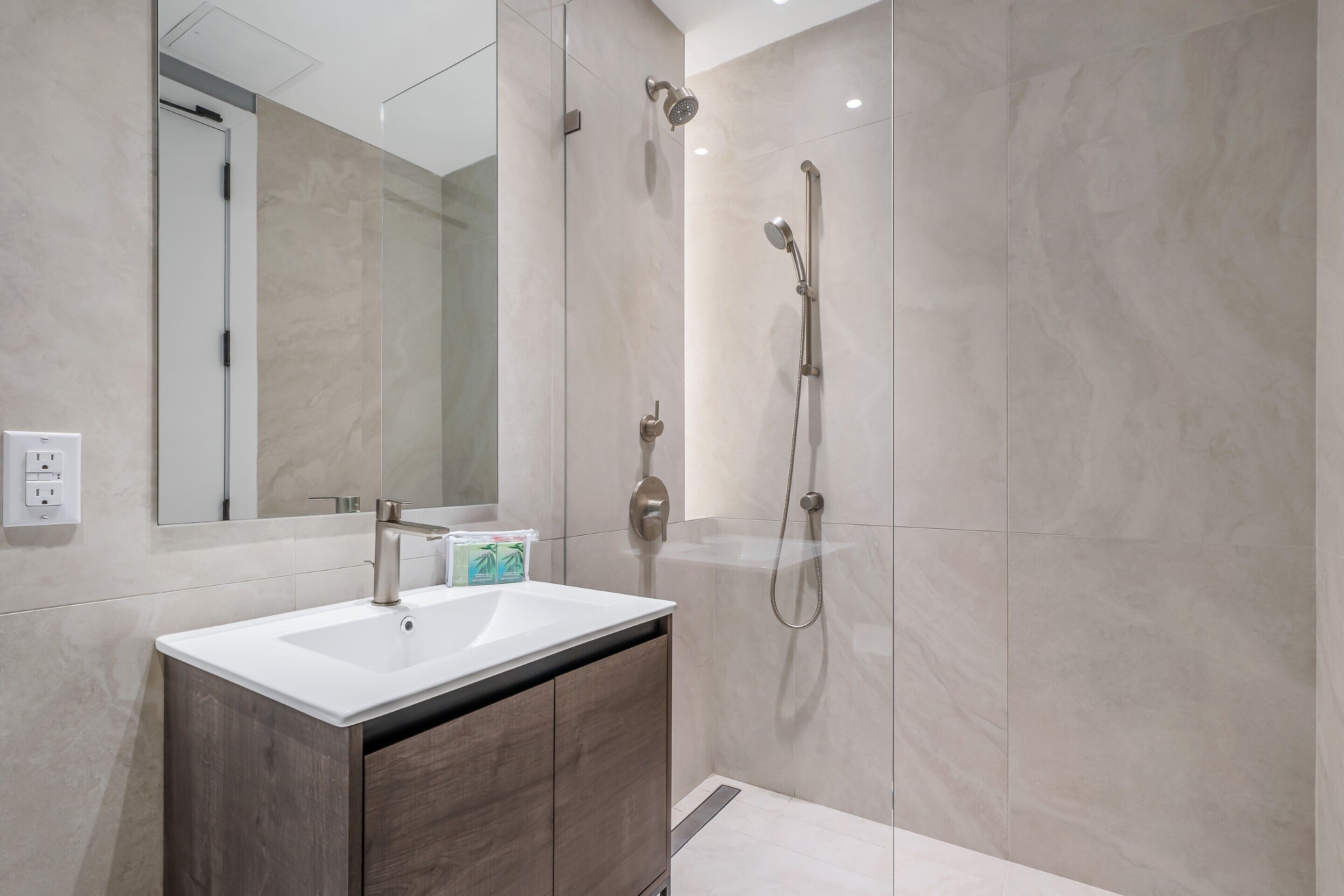 Un baño moderno con un espejo grande, un lavamanos blanco y una zona de ducha.