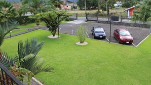 A parking area with three cars, surrounded by well-maintained grass and palm trees. - Apartment 8: Condos Vista al Volcan - Second Floor (La Fortuna)