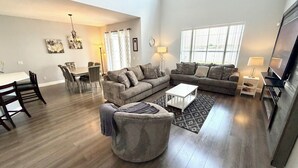 A spacious living room with a dining area, a sofa set, a coffee table, and a TV. - Relax in style! Close to parks - TVs every room - Modern kitchen - near golf. (Davenport)