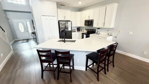 A modern kitchen with white cabinets, a large island with bar stools, and a stainless steel refrigerator. - Relax in style! Close to parks - TVs every room - Modern kitchen - near golf. (Davenport)