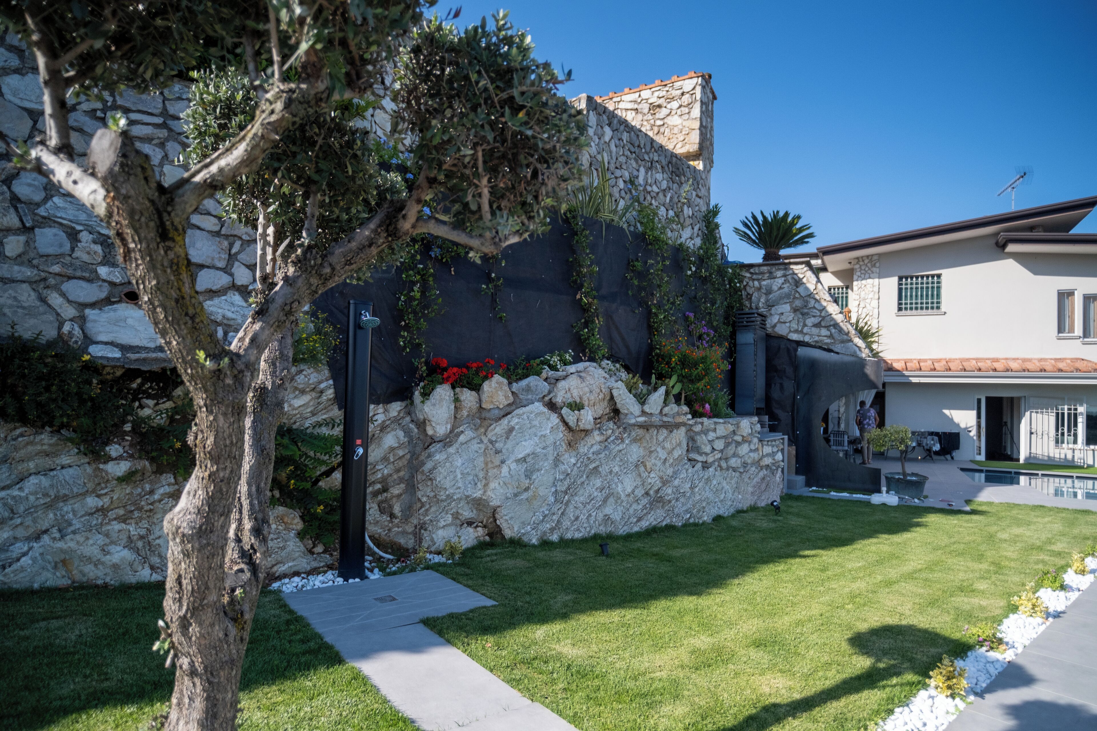 A stone wall with climbing plants, a tree, and a well-maintained lawn.
