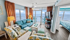 Amplia habitación con sofá, sillas, una mesita de centro y televisión. Cuenta con ventanas grandes con vista al mar.