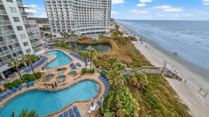 Un resort con un amplio espacio de piscina, una playa y un edificio de gran altura.