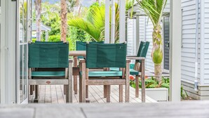 Een houten terras met groene fauteuils en een tafel, omringd door witte gebouwen en palmbomen.