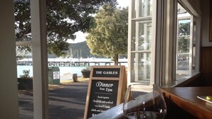 Een restaurant met uitzicht op een haven, een bordje met de tekst 'The Gables' diner, en een wijnglas op tafel.