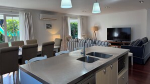 Een moderne keuken met een centraal eiland, een eethoek met stoelen, een bank, een televisie en een lamp.