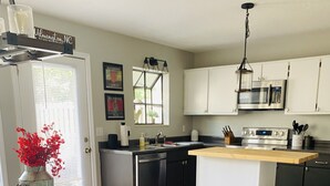 Una cocina con una isla de madera, armarios blancos, electrodomésticos de acero inoxidable y una silla tapizada en azul.