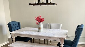 Una mesa de comedor con un banco, dos sillas, un florero con flores y una lámpara colgante.