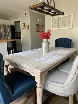A dining table with a rustic finish, surrounded by upholstered chairs with decorative buttons, a vase with red flowers, and a pendant light fixture above.