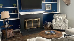 Una sala de estar con chimenea, televisor montado, sillón estampado y una mesa de centro.
