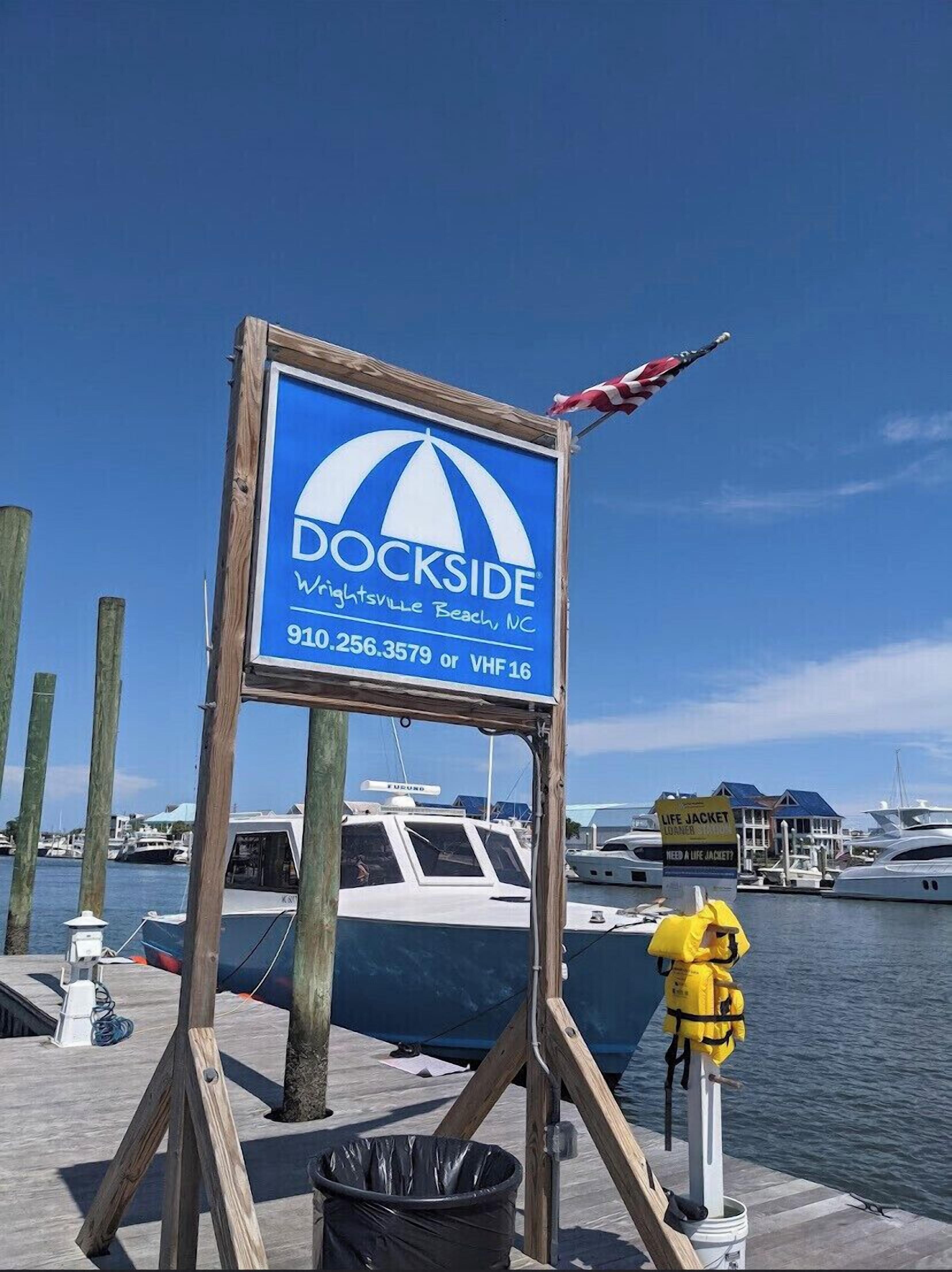 A sign for Dockside in Wrightsville Beach, NC, with contact information and a life jacket sign nearby.