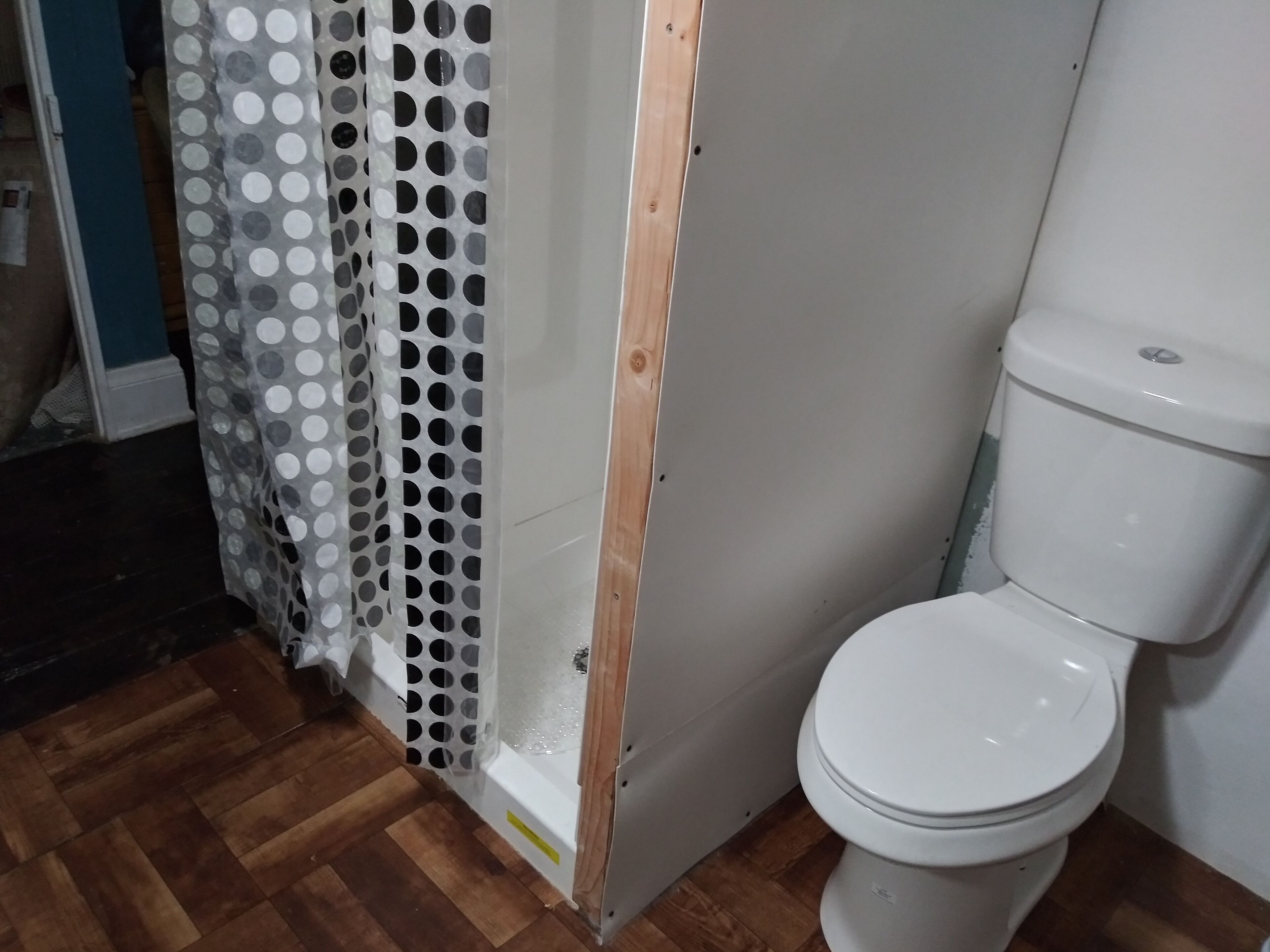 Un baño con inodoro blanco, cortina de ducha a lunares y suelo de madera.