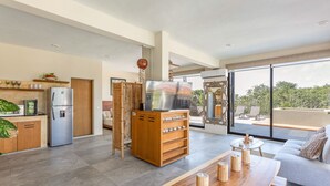 A modern kitchen with a large refrigerator, a wooden cabinet, and a flat-screen TV. There is a dining area with a wooden table and chairs, and a sofa with a view of the outdoors. - Luxury Penthouse Suite Private Pool X17 (Tulum)