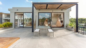 A modern outdoor patio with a glass table and benches, surrounded by potted plants and a wooden deck. - Luxury Penthouse Suite Private Pool X17 (Tulum)