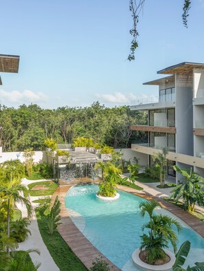 A modern pool area with a waterfall feature, surrounded by lush greenery and a clear blue sky.