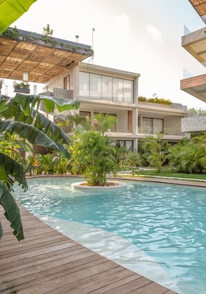 A modern hotel with a pool, surrounded by lush greenery and a wooden deck.