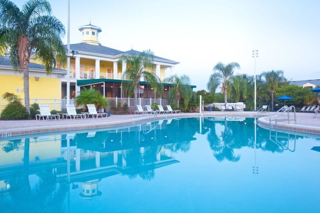 A swimming pool with lounge chairs and a building with a yellow facade and a tower.