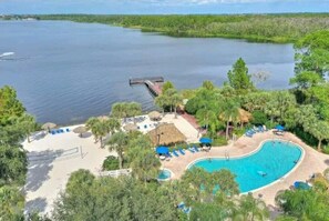 A resort with a swimming pool surrounded by palm trees and a dock extending into a lake.