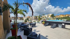 En tagterrasse med udendørs møbler, en swimmingpool og udsigt over lystbådehavn samt bygninger i baggrunden.