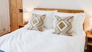 Un lit bien fait, avec une literie blanche et deux coussins décoratifs, une tête de lit en bois et des lampes de chevet.