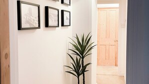 Un couloir avec des tableaux encadrés accrochés au mur, une plante en pot et une porte en bois au fond.