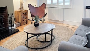 Un salon moderne avec une table basse ronde, un fauteuil en cuir et un canapé gris. On peut voir une cheminée et une plante en pot.