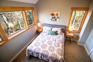 A bedroom with a large bed, two bedside tables, a nightstand, and a window with a view of trees. - Quiet & Peaceful (Galena)